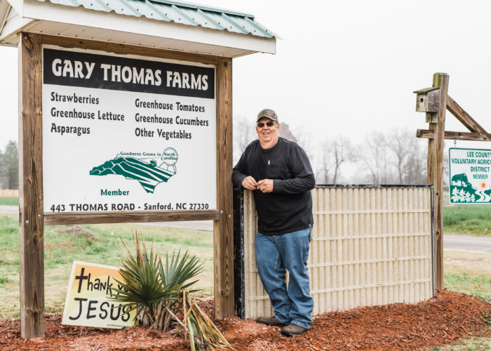 Farm owner stands smiling near farm's sign. Credit: Cooperative Extension